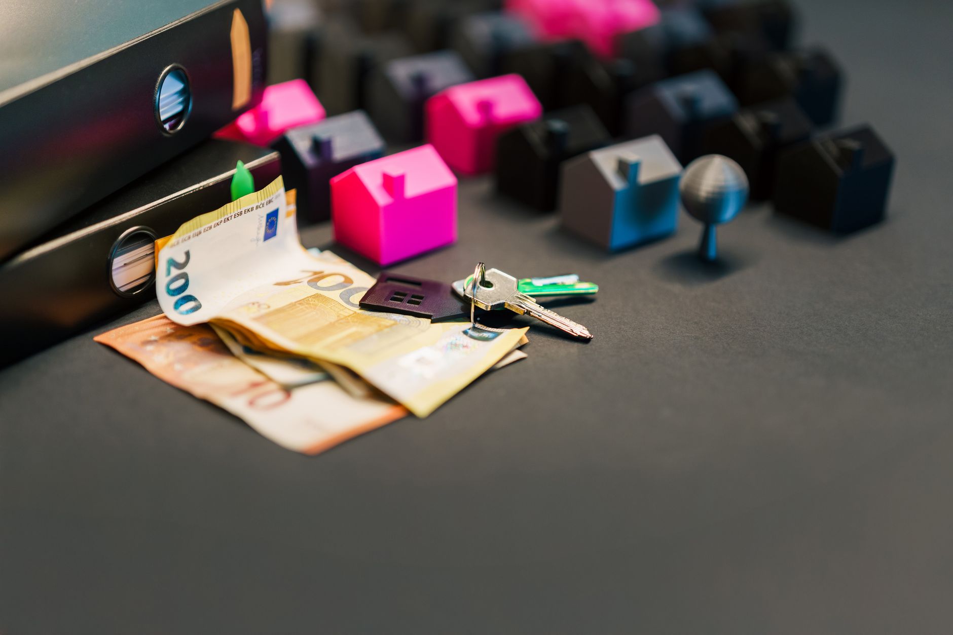Euro banknotes and house keys beside colorful Monopoly-style house pieces, symbolizing property investment finances.